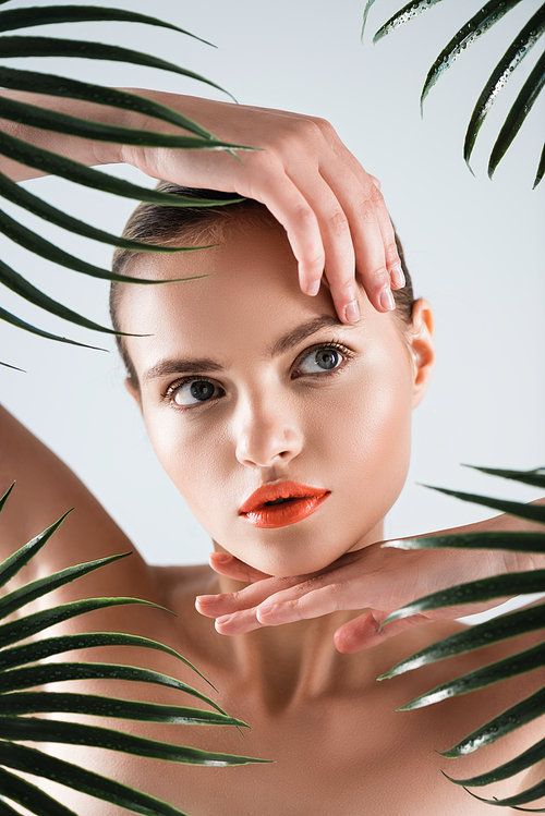 naked girl with makeup touching face near palm leaves on white