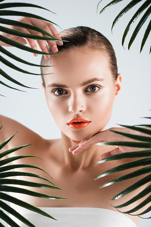 attractive woman touching face near palm leaves on white