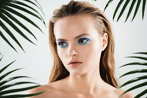 beautiful woman with blue eye shadow near palm leaves on white