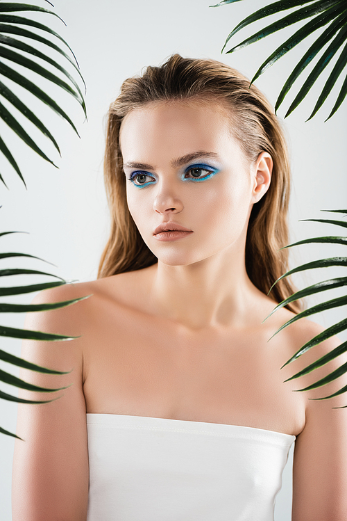 beautiful young woman with with blue eye shadow near palm leaves on white