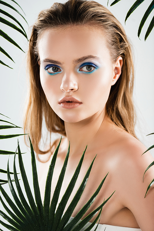 beautiful woman with makeup near palm leaves on white