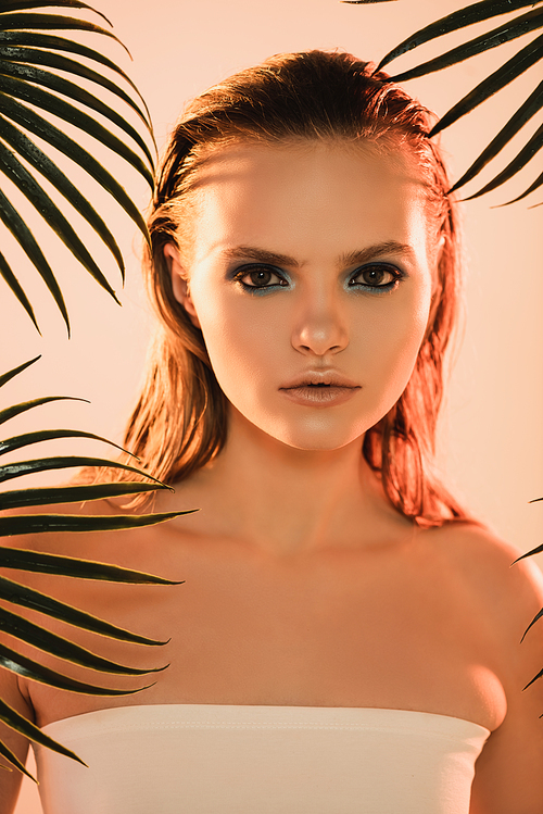 beautiful woman with makeup  near palm leaves on beige