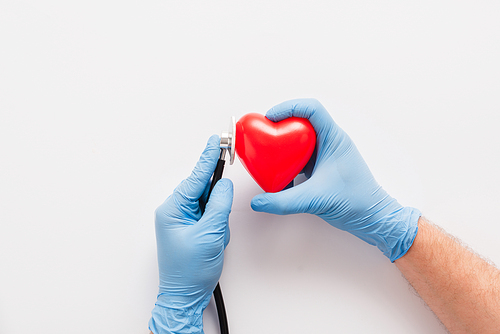cropped view of doctor in latex gloves examining red heart with stethoscope on white background