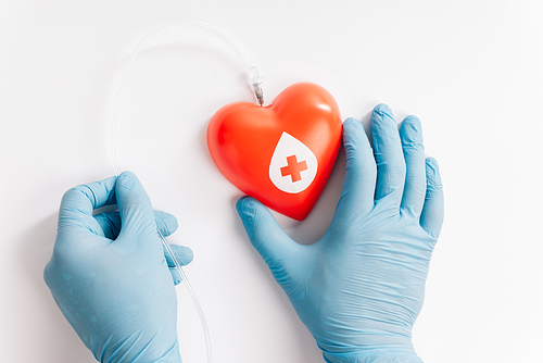 cropped view of male hands in latex gloves holding red heart with catheter on white, blood donation concept