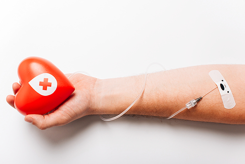 cropped view of male hand with red heart and catheter on white, blood donation concept