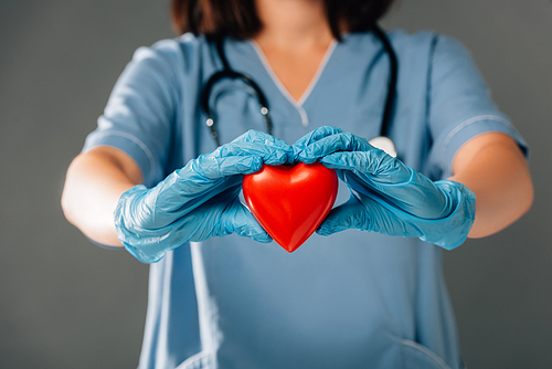 cropped view of doctor with stereoscope in latex gloves holding red heart isolated on grey