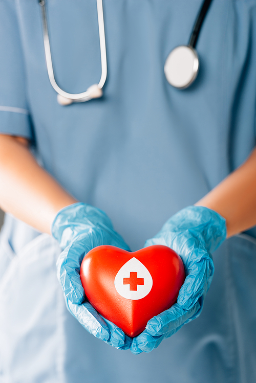cropped view of doctor with stereoscope holding red heart, blood donation concept