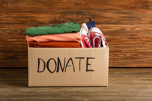 cardboard box with donated clothes and footwear on wooden background, charity concept