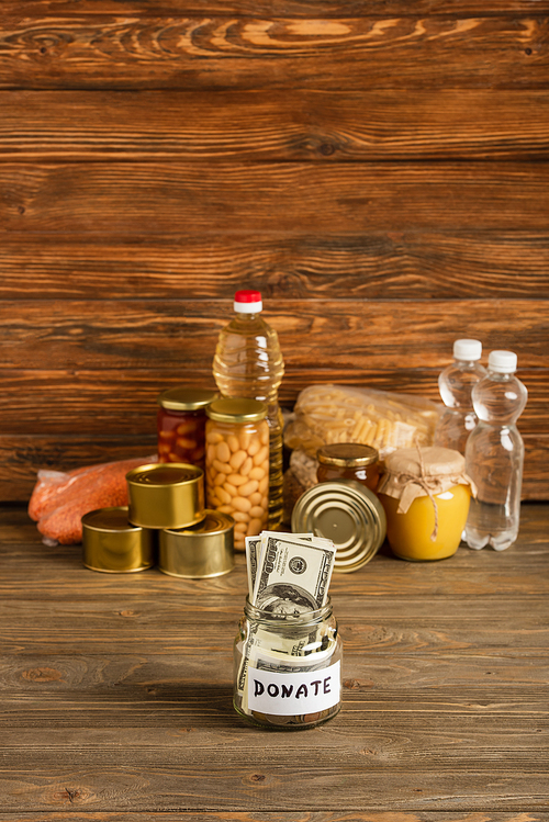 selective focus of jar with money and donated food on wooden background, charity concept