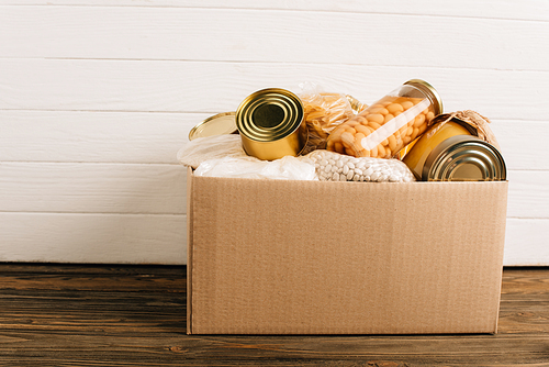 cardboard box with donated food on wooden background, charity concept