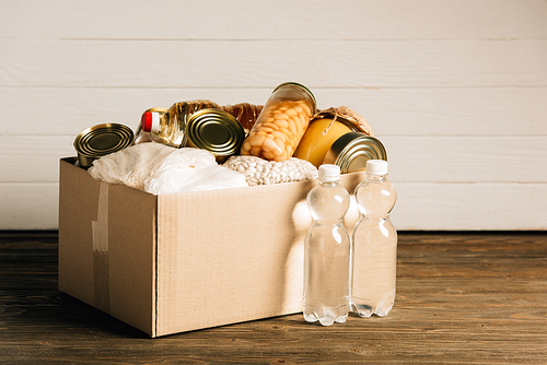 cardboard box with donated food and water on wooden background, charity concept