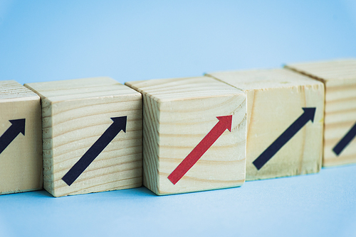 close up view of wooden blocks with black and red arrows on blue background, leadership concept