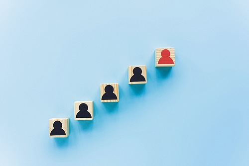 top view of wooden blocks with black and red human icons on blue background, leadership concept
