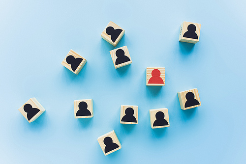 top view of wooden blocks with black and red human icons scattered on blue background, leadership concept