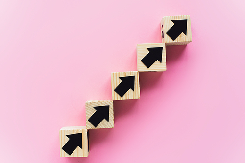 top view of wooden blocks with black arrows on pink background, business concept