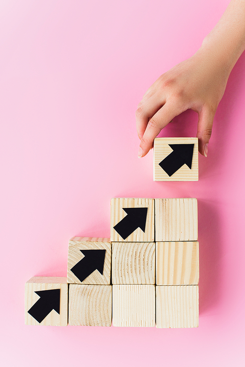 partial view of hand near wooden blocks with black arrows on pink background, business concept