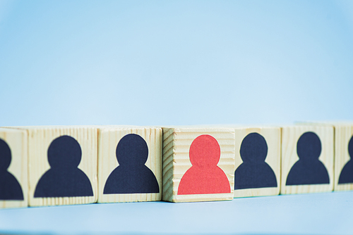 row of wooden blocks with black and red human icons on blue background, leadership concept