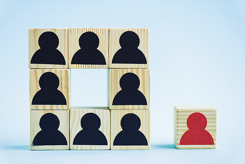 square of wooden blocks with black human icons and red piece on blue background, leadership concept