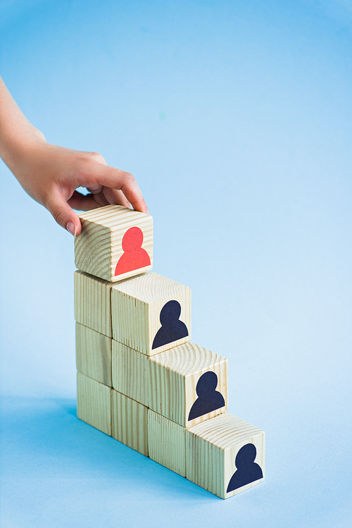 cropped view of hand touching pyramid of wooden blocks with black and red human icons on blue background, leadership concept