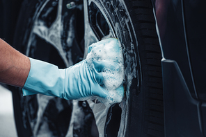 partial view of car cleaner wiping wheel with rag