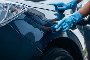 partial view of car cleaner in rubber gloves polishing car