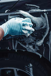 partial view of car cleaner washing black car with sponge and detergent