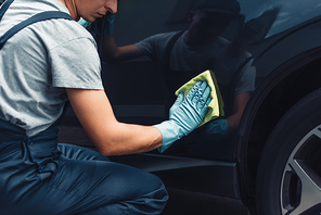 partial view of car cleaner polishing black car with rag