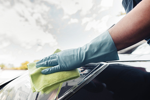 cropped view of car cleaner in rubber glove wiping car with rag