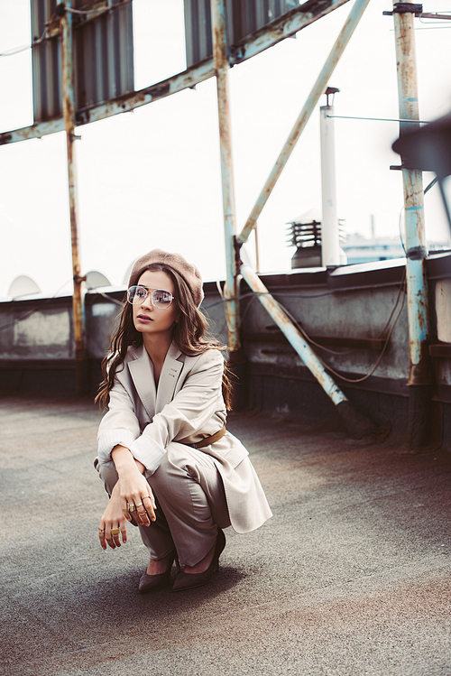 trendy girl posing in beige suit and beret on urban roof