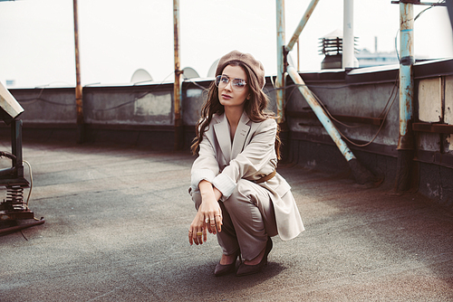 attractive trendy girl posing in beige suit and beret on urban roof