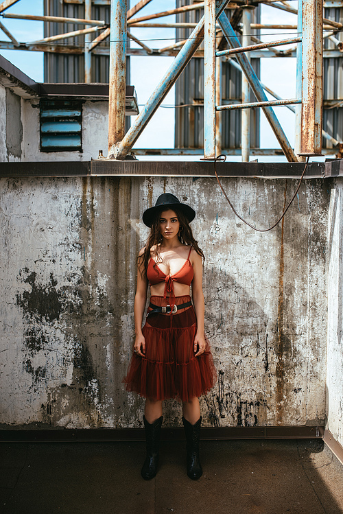 attractive trendy girl posing in red skirt, bra and hat on roof