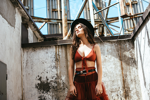 stylish woman posing in red skirt, bra and hat on roof