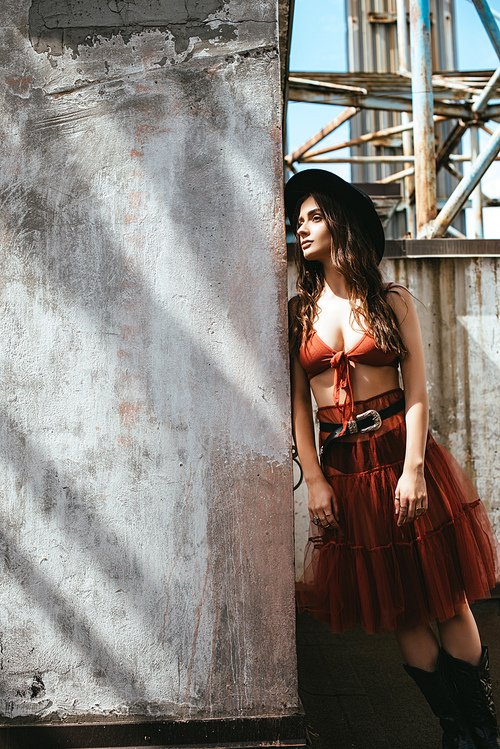 attractive stylish woman posing in red skirt, bra and hat on roof