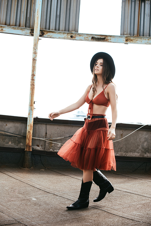 attractive stylish woman posing in red skirt, bra and hat on roof