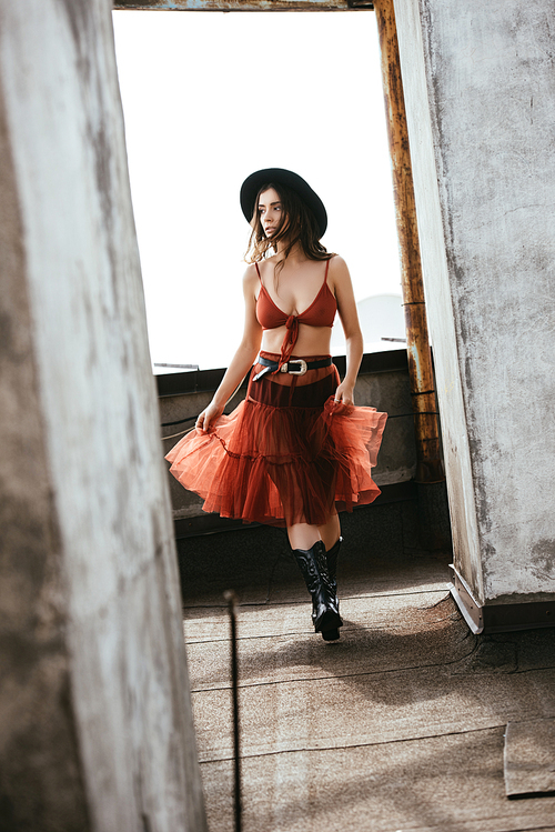 beautiful woman posing in red skirt, bra and hat on roof