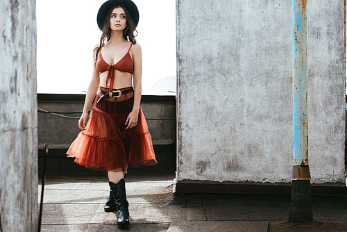 attractive woman posing in red skirt, bra and hat on roof