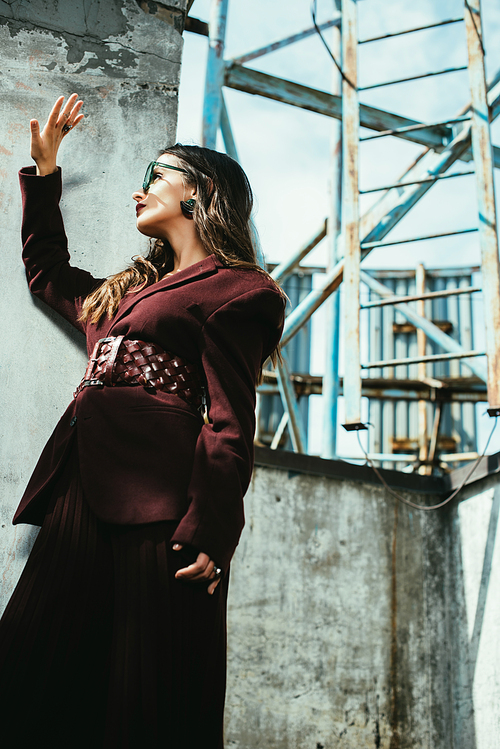 fashionable woman posing in trendy burgundy suit and sunglasses on urban roof