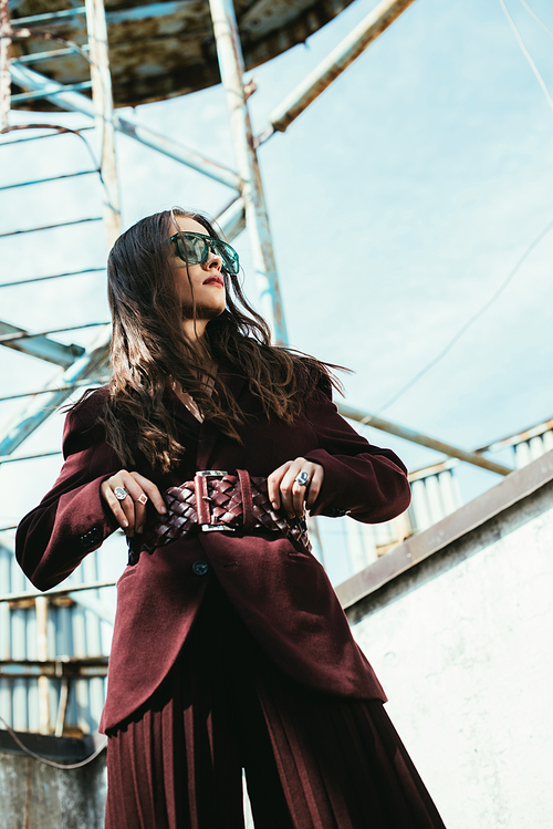 fashionable model posing in trendy burgundy suit and sunglasses on urban roof