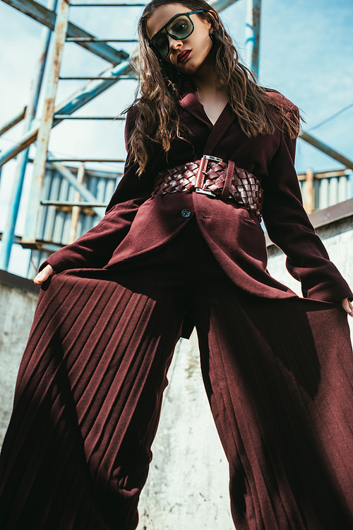 elegant model posing in trendy burgundy suit and sunglasses on urban roof