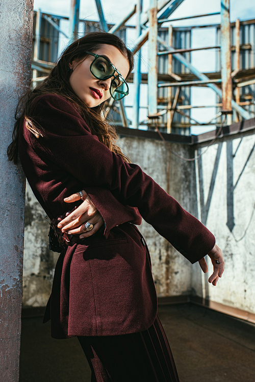 fashionable woman posing in trendy burgundy suit and sunglasses on urban roof