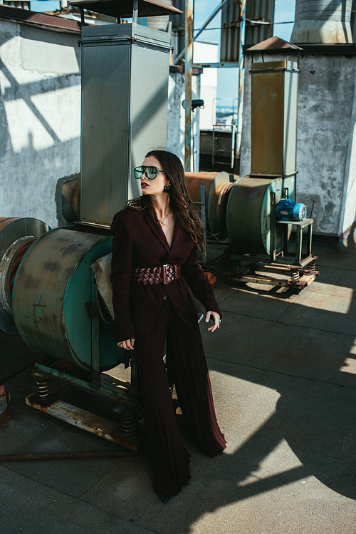 stylish elegant woman posing in trendy burgundy suit and sunglasses on urban roof