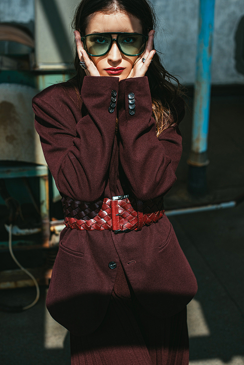 elegant young woman posing in trendy burgundy suit and sunglasses on urban roof