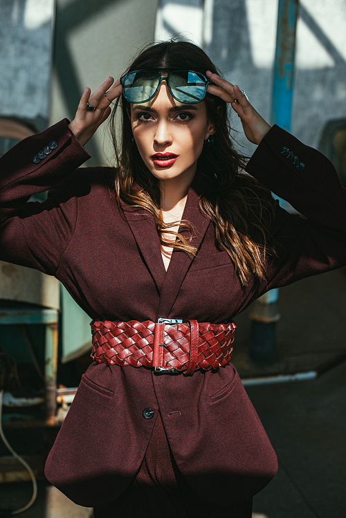 fashionable elegant woman posing in trendy burgundy suit and sunglasses on urban roof