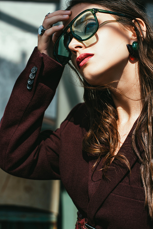 fashionable woman posing in trendy burgundy suit and sunglasses on urban roof