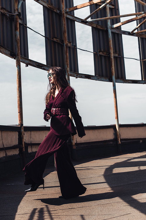 fashionable elegant woman posing in trendy burgundy suit and sunglasses on urban roof