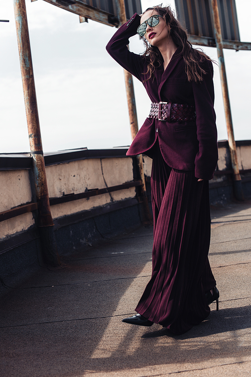 stylish woman posing in trendy burgundy suit and sunglasses on urban roof