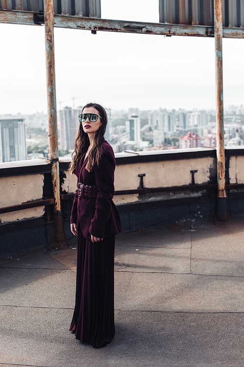 stylish elegant woman posing in trendy burgundy suit and sunglasses on urban roof