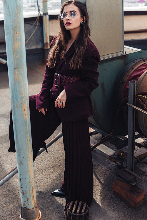 stylish elegant girl posing in trendy burgundy suit and sunglasses on urban roof