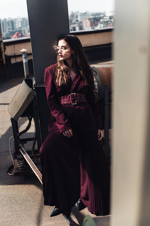 stylish woman posing in trendy burgundy suit and sunglasses on urban roof