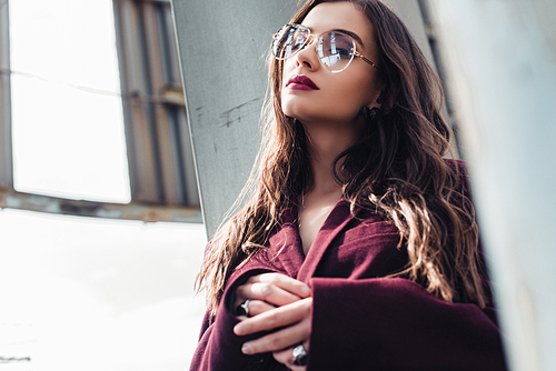 elegant young woman posing in trendy burgundy suit and sunglasses on urban roof